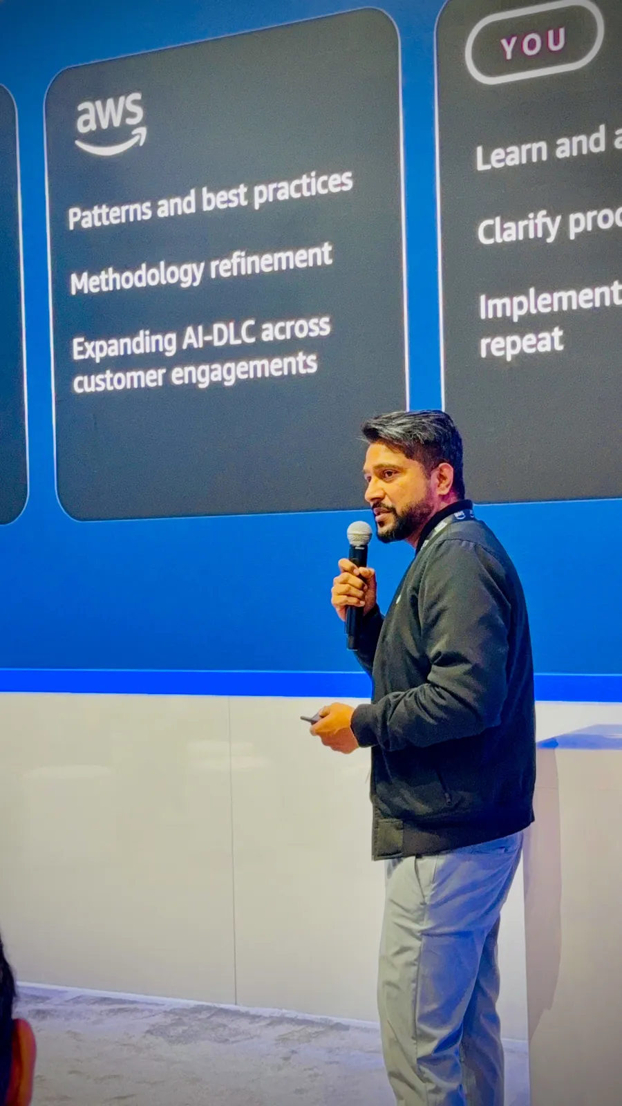 Ganesh Raam beside a slide of what AWS and the customer team each bring